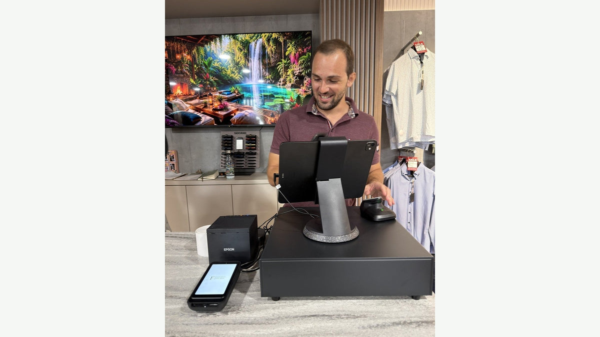 Daniel Perera of ShopiCraft at a Shopify POS Pro countertop setup with iPad stand, Epson receipt printer, card reader and POS Go in an Irish menswear shop