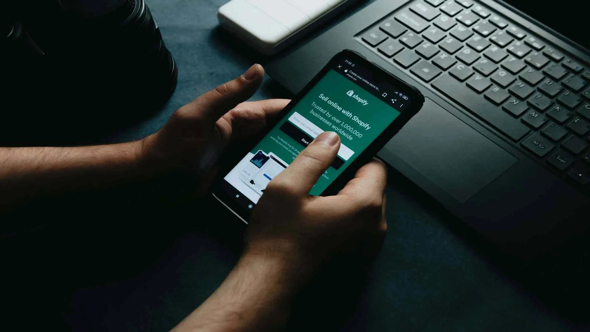 Start selling on Shopify image with a person holding a mobile phone about to set up a Shopify store through the Shopify homepage.